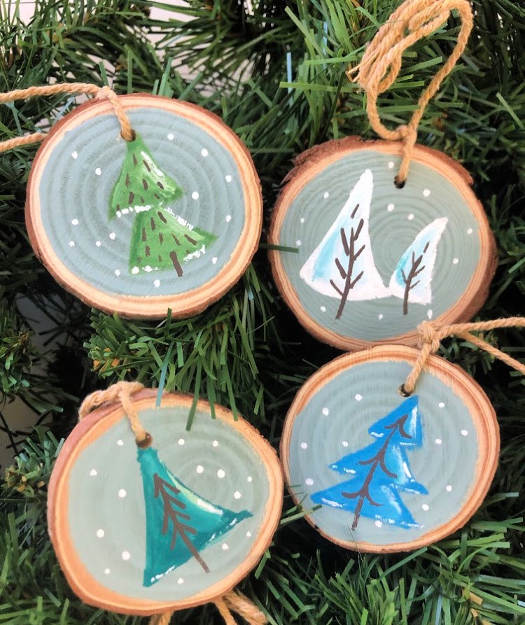 image shows 4 circular wood slices with paintings of winter fir trees.